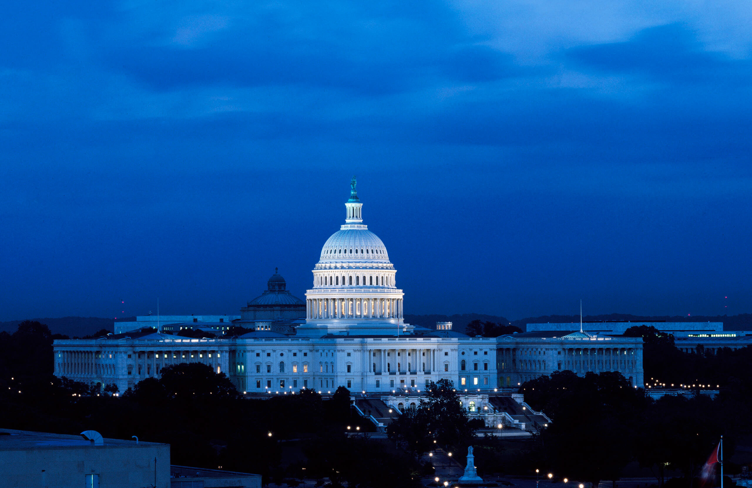 The U.S. Capitol at night. The Dome glows white against a dark blue sky.